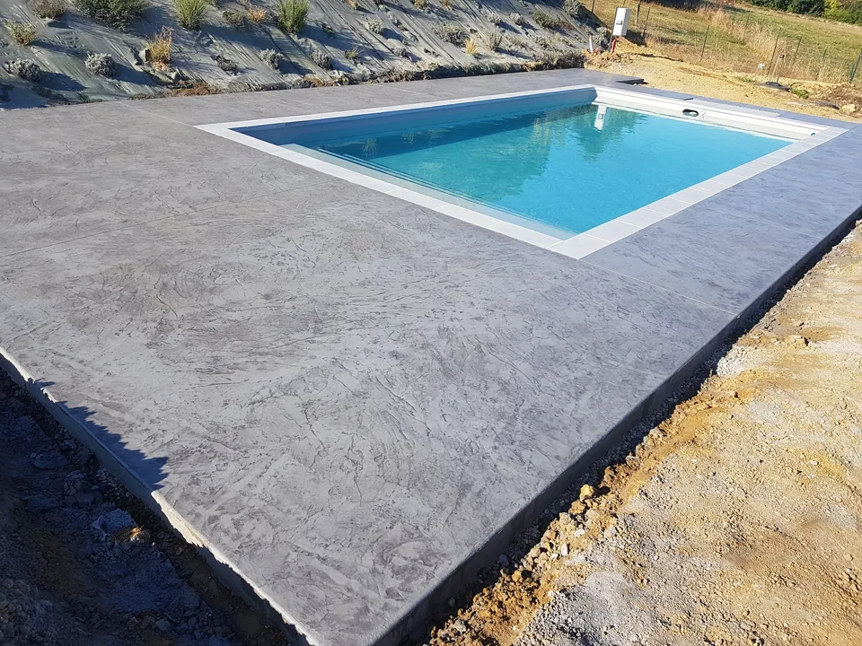 Dallage en béton imprimé gris à effet pierre autour d’un bassin rectangulaire.