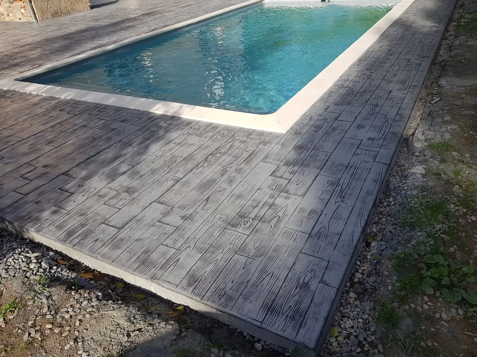 Détail du dallage en béton imprimé à motif bois le long du bassin.