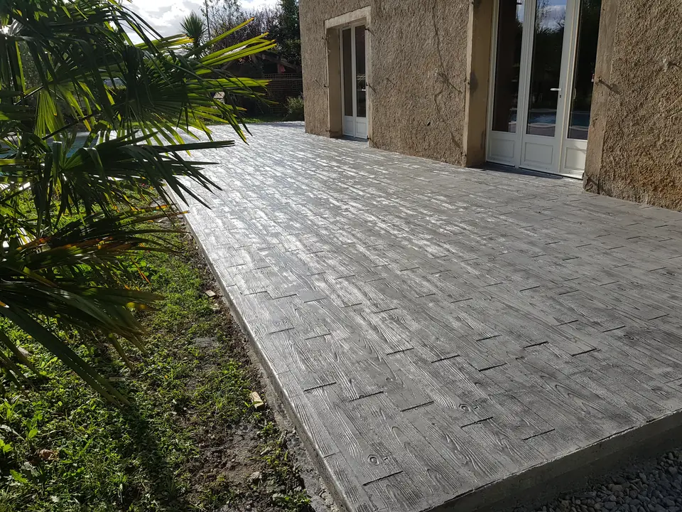 Terrasse en béton imprimé gris à motif bois le long d’une maison en pierre.