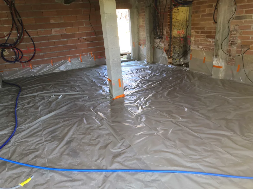 Pièce en rénovation : film polyane posé sur le sol avant la nouvelle dalle, entre des murs de brique.